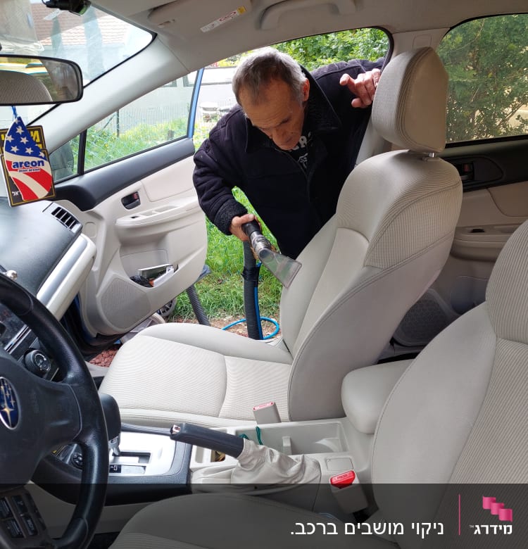 אדם מנקה מושב רכב עם שואב אבק